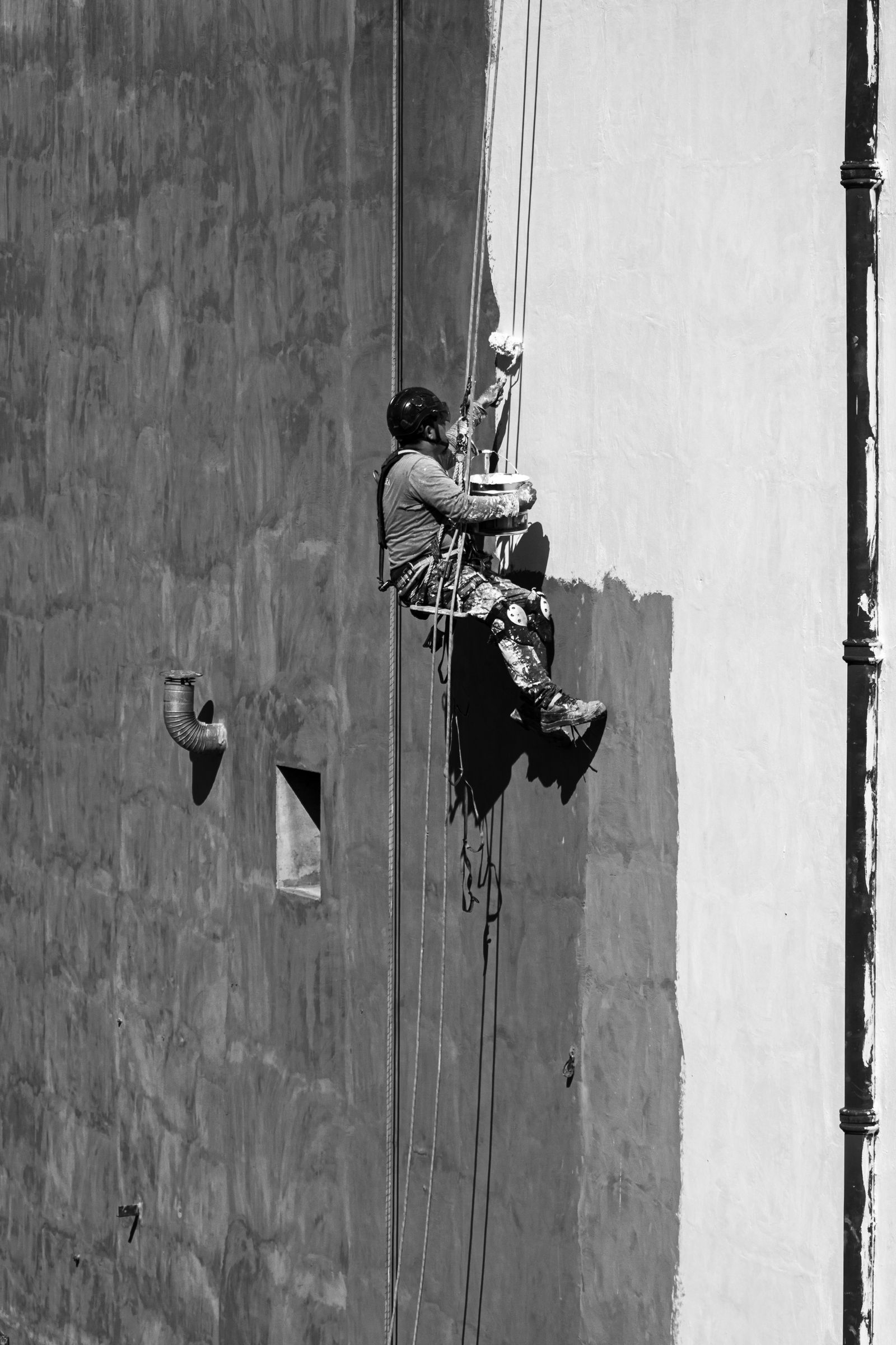 Técnico suspendido con cuerdas pintando una fachada